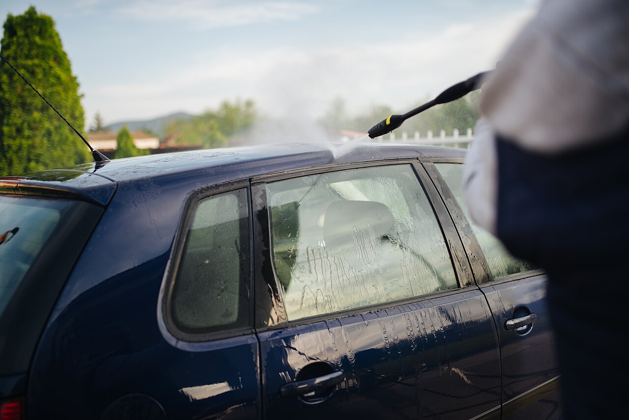 Pessoa lavando carro com lavadora de alta pressão em garagem residencial