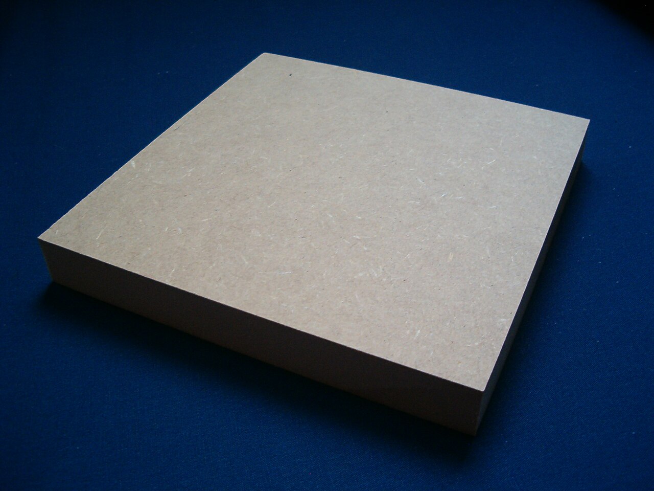 Chapa de MDF cru sobre fundo azul, mostrando a espessura e a textura do material usado na mesa dobradiça de parede