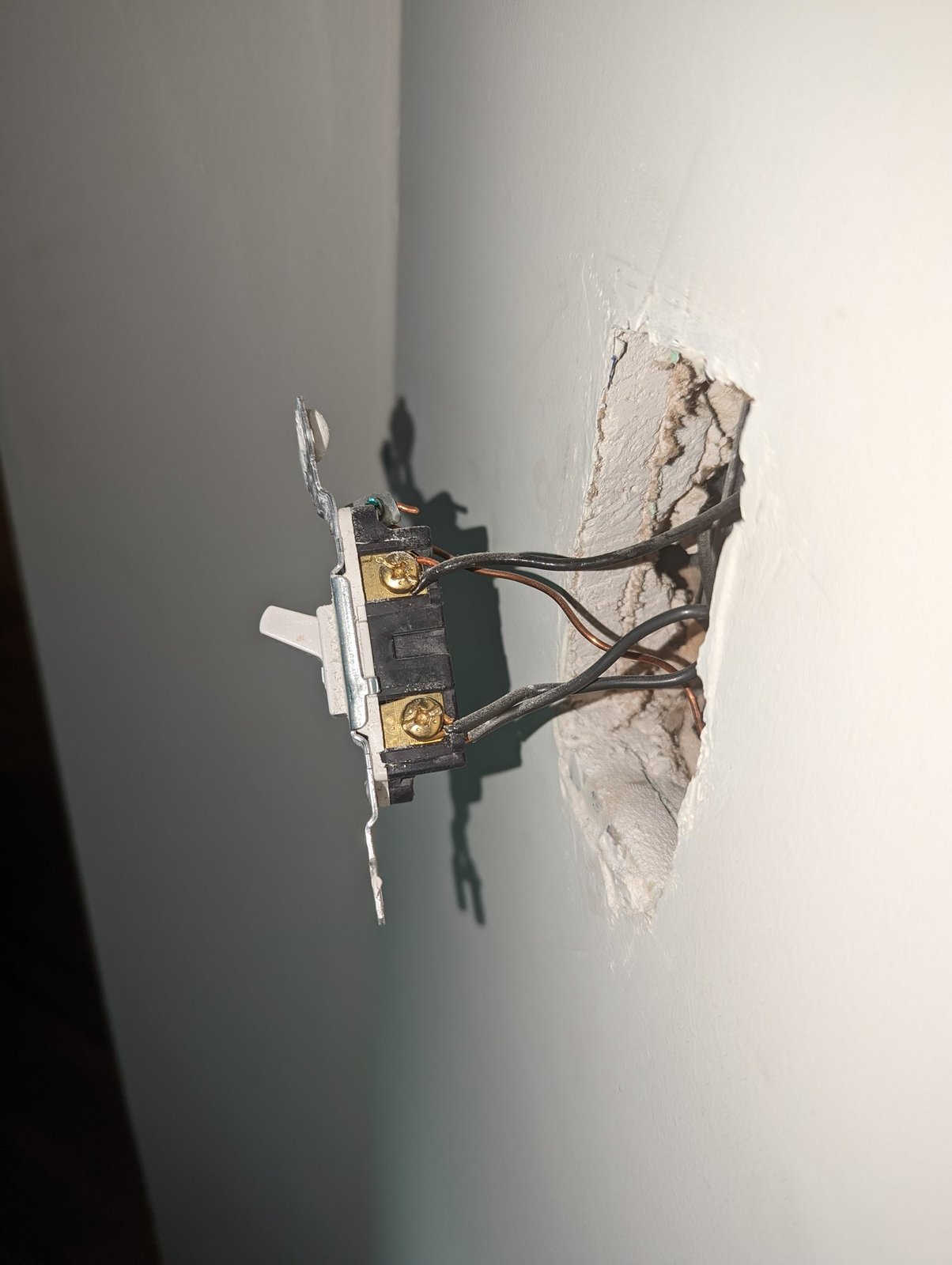 Interruptor de luz retirado da caixa de embutir, mostrando os fios conectados aos terminais