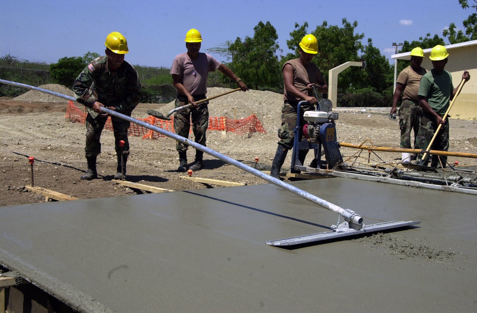 Trabalhadores usando régua e desempenadeira para nivelar e alisar a superfície de um piso de concreto recém-lançado