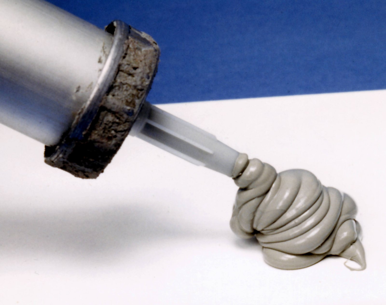 Cordão de silicone extrudado de uma pistola de aplicação, mostrando a textura e consistência típica do produto