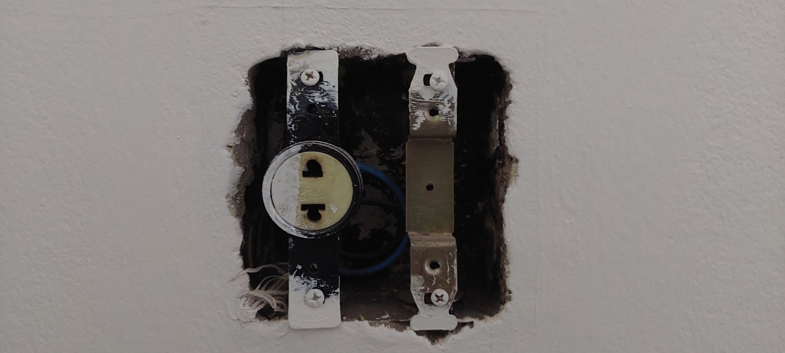Tomada elétrica removida da parede, mostrando fios expostos antes da verificação com detector de tensão