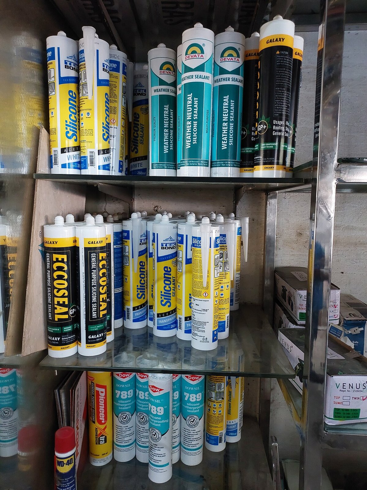 Prateleira com diversos tubos de silicone à venda, mostrando rótulos e embalagens de diferentes marcas